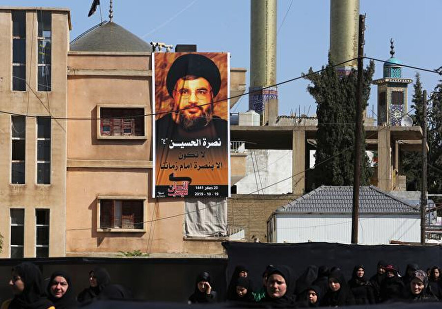Nasrallah'ın televizyon yayınlanan konuşması sırasında dinleyicilerin arkasında duvarlara asılmış posterleri görülüyor.