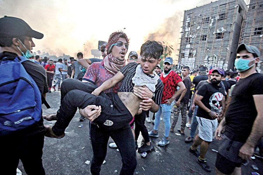 Gösteriler sırasında yaralanan arkadaşını kucağında hastaneye taşıyan Iraklı.