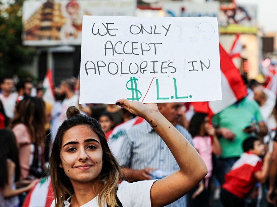 Lübnan'da bir protestocu elinde tuttuğu pankartla, devleti yönetenlerin özürlerinin ancak borçlar kapatıldığında kabul edileceğini belirtiyor.