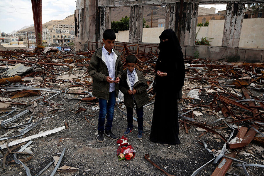 Yemen'de babalarının çatışmada öldüğü yere çiçek bırakıp dua eden bir aile.