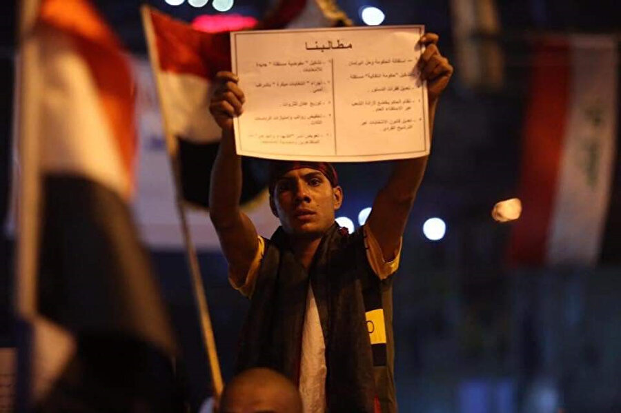 Iraklı bir protestocu elinde pankartla görünüyor.