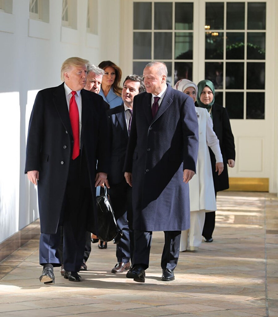 Cumhurbaşkanı Erdoğan ile Başkan Trump, Beyaz Saray koridorlarında ilerliyor. Hemen arkalarında ise eşleri takip etmekte.