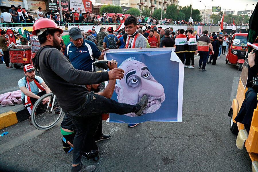 Hükümet karşıtı gösteriler sırasında Başbakan Adil Abdulmehdi'nin posterlerini tekmeleyen protestocular.