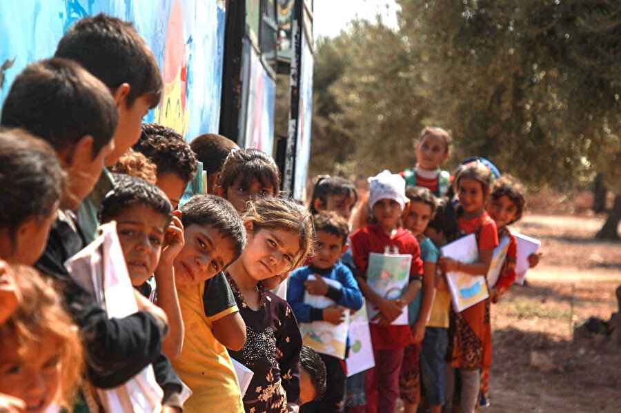 15 Eylül 2019'da çekilen bu fotoğrafta yerinden edilmiş çocuklar, Suriye'nin kuzeybatısındaki Hazano köyünde sınıfa dönüştürülen bir otobüsün dışında sıralarını bekliyor.