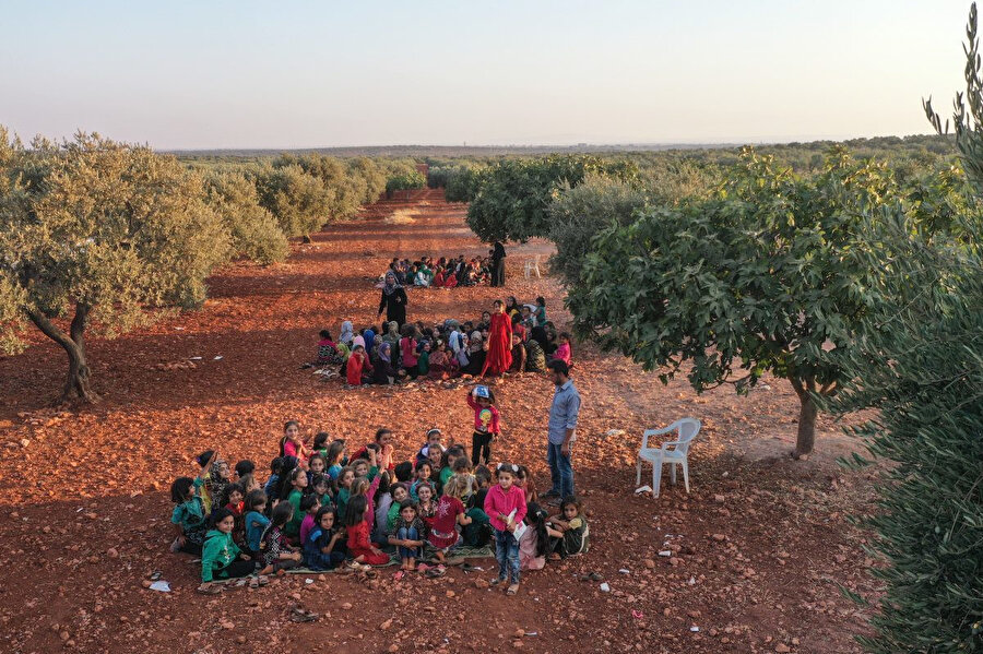 18 Eylül 2019'da Suriyeli çocuklar, İdlib kentine bağlı Killi köyünde açık havada, zeytin ağaçlarının altında ders dinliyorlar.