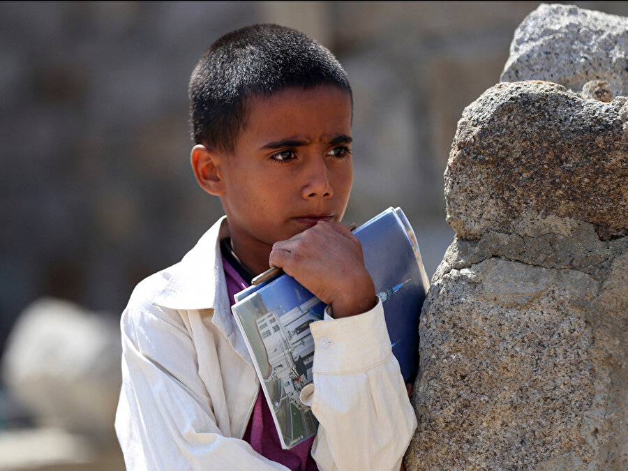 Yemenli bu çocuk, yapımı henüz tamamlanmamış okulunun yanındaki ağacın altında açık havada yapılan derse katılmak için defteri elinde bekliyor.