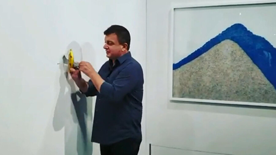 Aç sanatçı 120 bin dolara satılan duvara bantlanmış muzu yemek için duvardan alırken