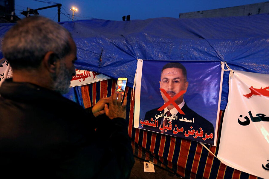 Irak'ta devam eden gösteriler sırasında Bina Koalisyonunun başbakan adayı Basra Valisi Esad İdani'nin posterinin fotoğrafını çeken bir Iraklı.