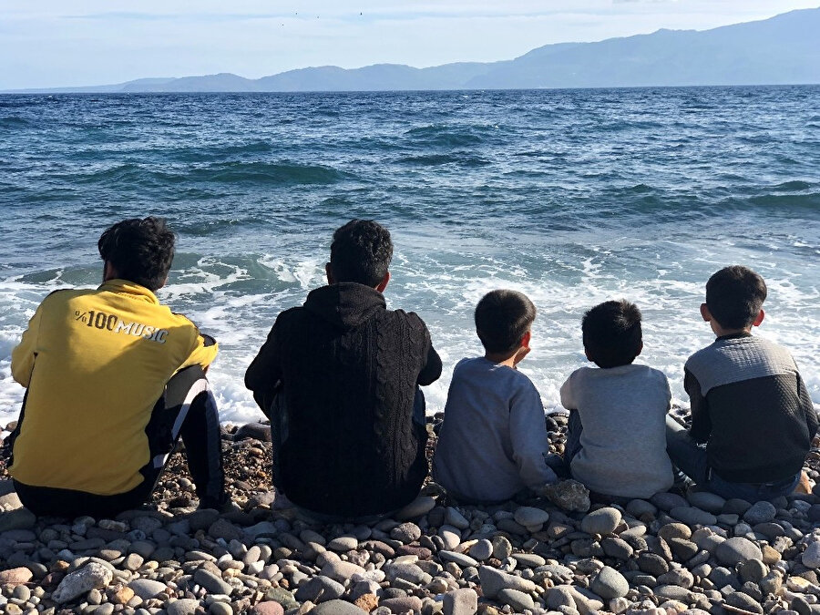 Denizden Yunanistan'a geçmek isteyen çocuklar sahilde otururken görünüyor.