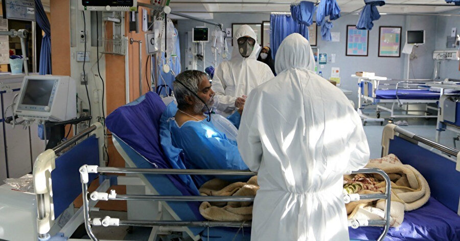 Bir koronavirüs hastasına tedavi uygulayan özel kıyafetli, maskeli sağlık çalışanları.