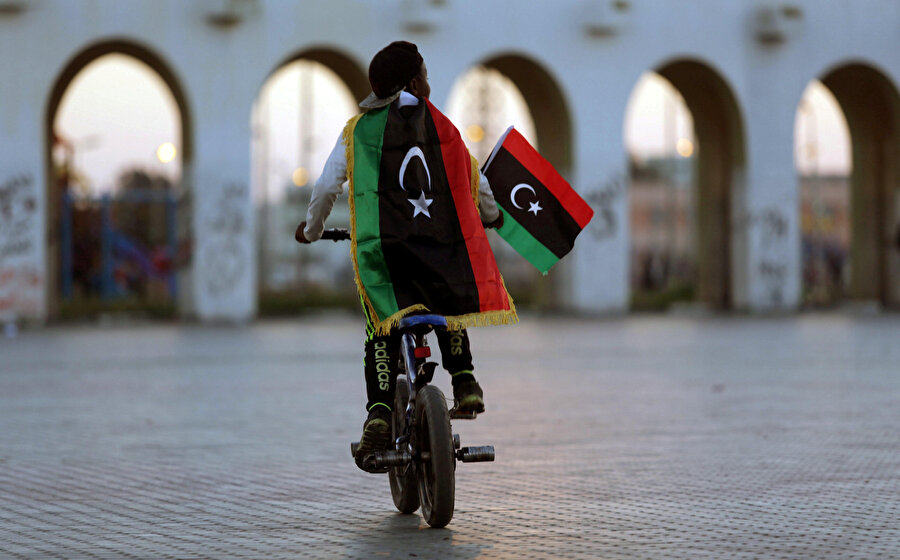 Bir çocuk Libya bayrağıyla bisiklet sürerken görünüyor.