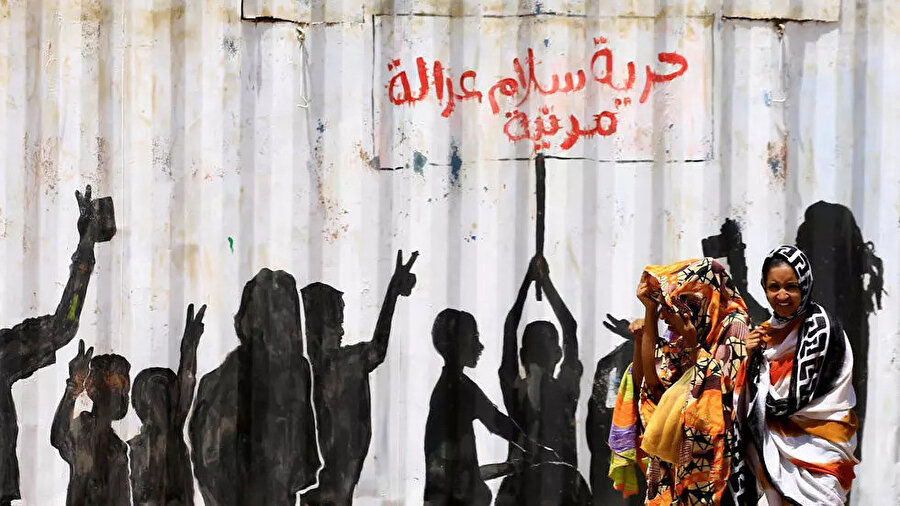 Sudan'ın başkenti Hartum'da "Özgürlük, Barış, Adalet ve Siviller" yazılı grafitinin önünden geçen kadınlar.