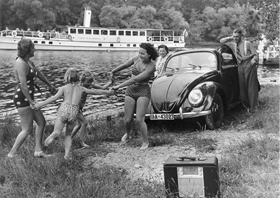 KdF reklamı: “KdF-Wagen ve radyo alıcısıyla nehir kenarında oynayan bir aile". KdF, Nazi Almanya’sının halk için kurduğu eğlence organizasyonuydu.