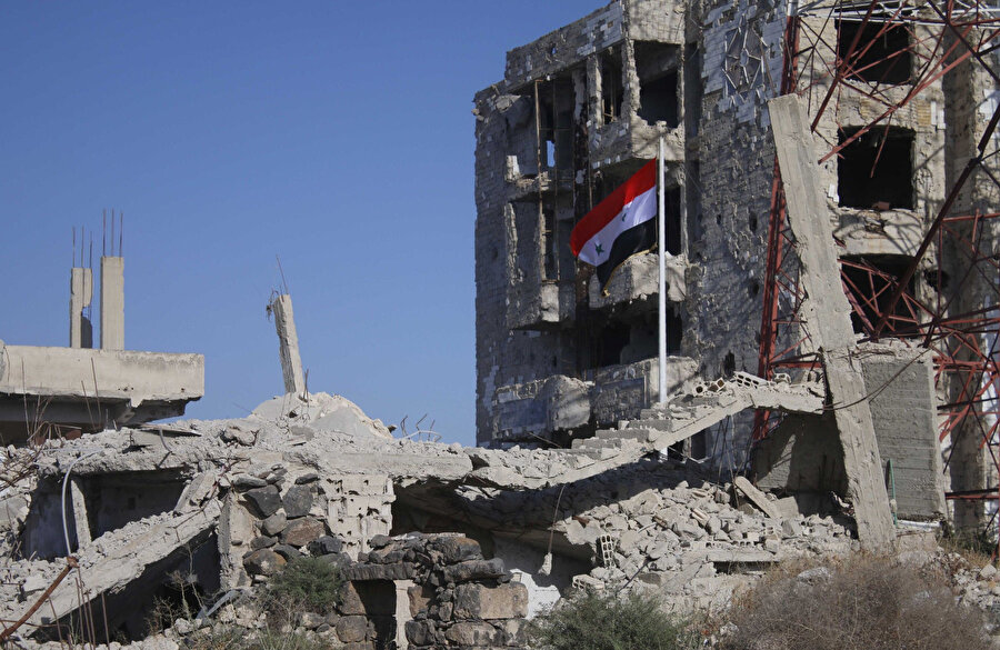 Dera'da yıkıntıların arasında dalgalanan rejim bayrağı.