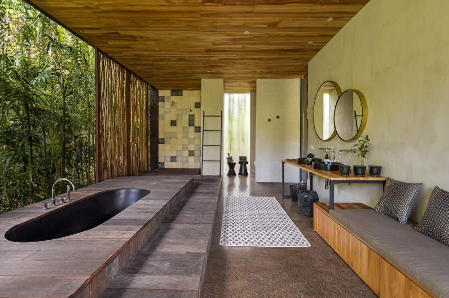 Bambu duvarlarla çevrili banyoda, siyah gömme bir küvet bulunuyor.