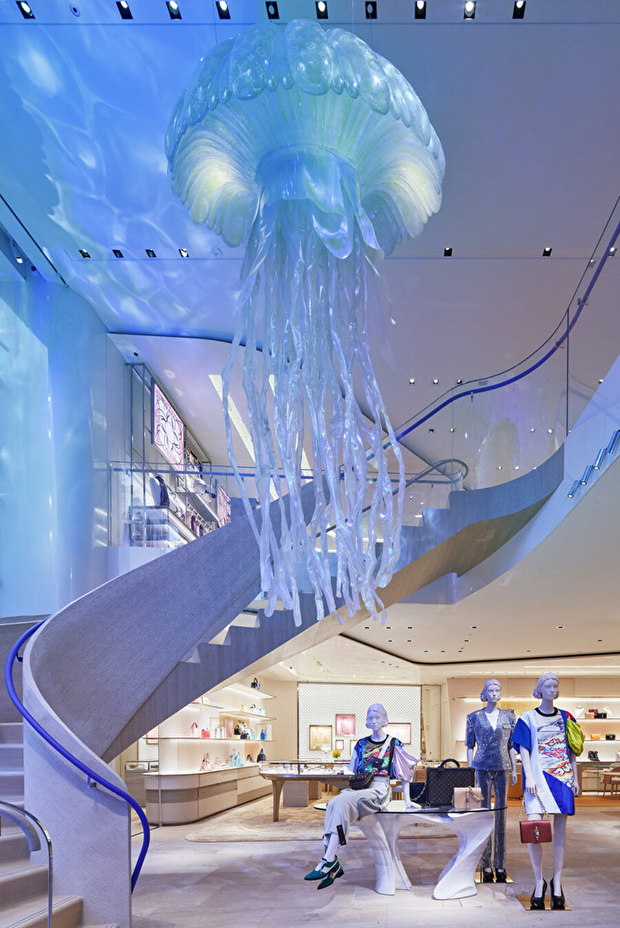 Mağazanın girişinde; ahşap ve cam malzeme paletinden ve kavisli yüzeylerden oluşan merdivene monogram detaylı devasa denizanaları eşlik ediyor.