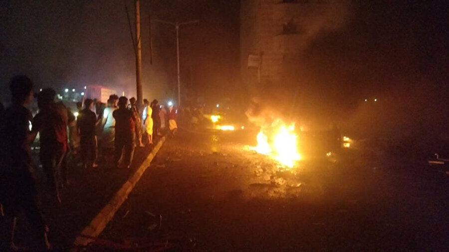 Yoldan geçenler, Yemen'deki Aden uluslararası havaalanının dışında patlamanın meydana geldiği yerde arabaların yanmasını izliyor.

