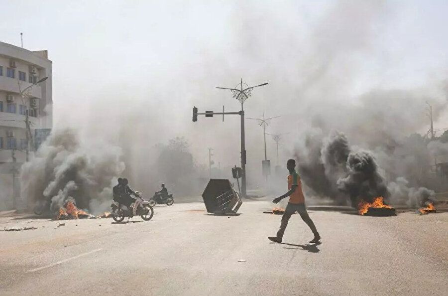 Ordunun rolünü destekleyen bir grup genç göstericinin Başkan Roch Christian Kabore'u protesto ettiği Ouagadougou'daki merkezi caddelerde yanan barikatların önünde bir adam geçiyor, 23 Ocak 2022.