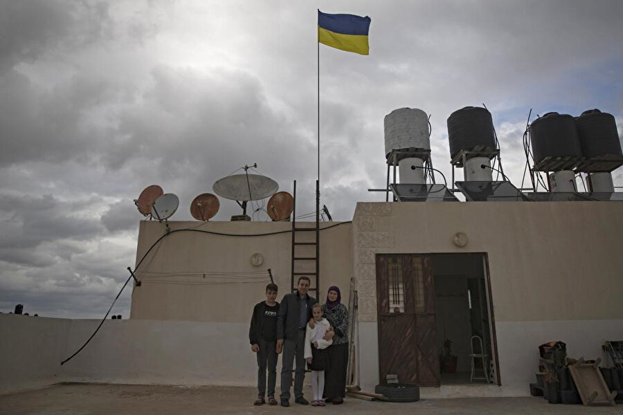 Ukraynalı Oksana el-Astal, 13 Mart 2022 Pazar, Gazze Şeridi'nin güneyindeki Han Yunus’taki evlerinin çatısında Ukrayna bayrağı dalgalanırken bir fotoğraf için poz verirken Filistinli kocası ve çocuklarıyla birlikte duruyor. (AP Fotoğrafı/ Halil Hamra)