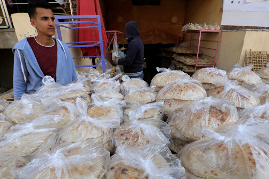 Kahire'nin güneydoğusundaki Mokattam semtindeki bir fırının önünde Mısırlı bir fırıncı, Rusya'nın Ukrayna'yı işgalinden bu yana Mısır'da temel gıda fiyatlarının artması nedeniyle Mısır'da bir fırının önünde poşet ekmekleriyle müşterilerini bekliyor. (REUTERS/Amr Abdullah Dalsh)