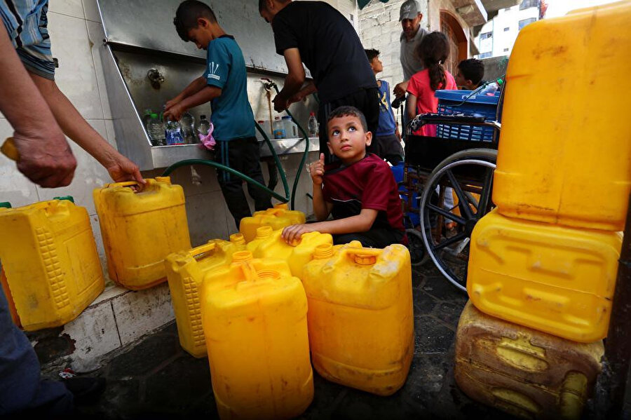 Gazze'de temiz içme suyu doldurmak için çocuklar çeşmelerin başında plastik bidonlarla toplanıyor.