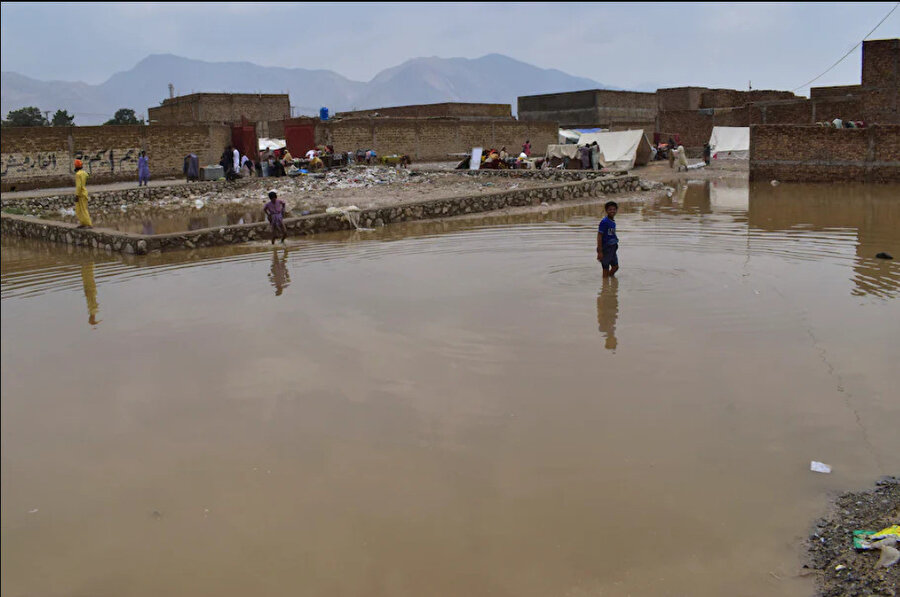 Quetta kentinin eteklerinde çocuklar sular altında kalan bir bölgeden geçiyor.