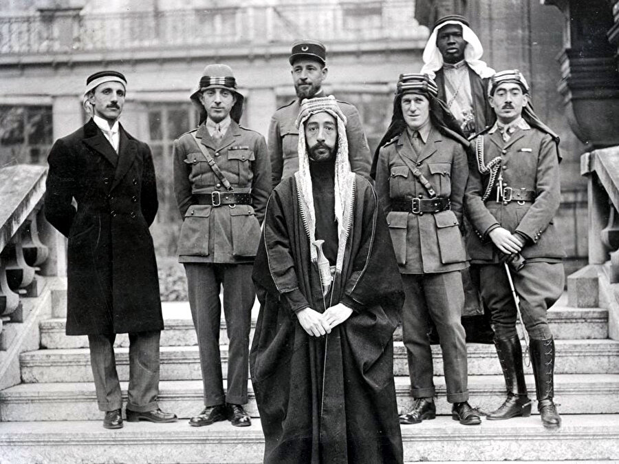 Emir Faysal, iki yıl sonra Irak’ı birlikte yönetmeye başlayacağı çekirdek kadroyla birlikte Paris Barış Konferansı'nda (1919-1920); (soldan sağa) geleceğin Irakı'nın Savunma Bakanı Rüstem Haydar, geleceğin Irakı’nın başbakanı Nuri Said, Emir Faysal, Fransız komutan Kaptan Rosario Pisani (Faysal’ın tam arkasında), Arabistanlı Lawrence, Kaptan Tahsin Kadri ve Faysal’ın ismi bilinmeyen siyahî kölesi.
