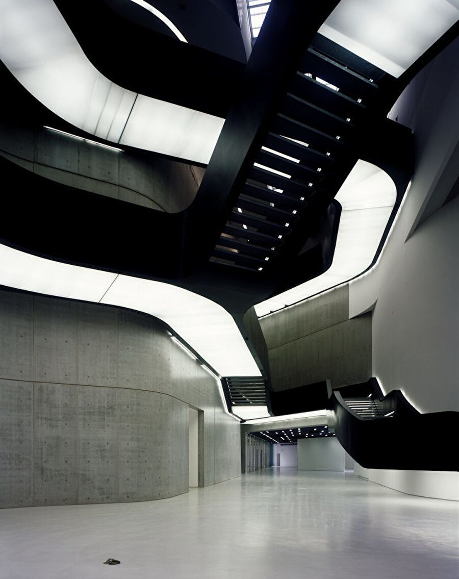 Merdiven korkulukları boyunca gizli ışık bantları beton duvarlarda yüzen ışık efekti oluşturuyor.