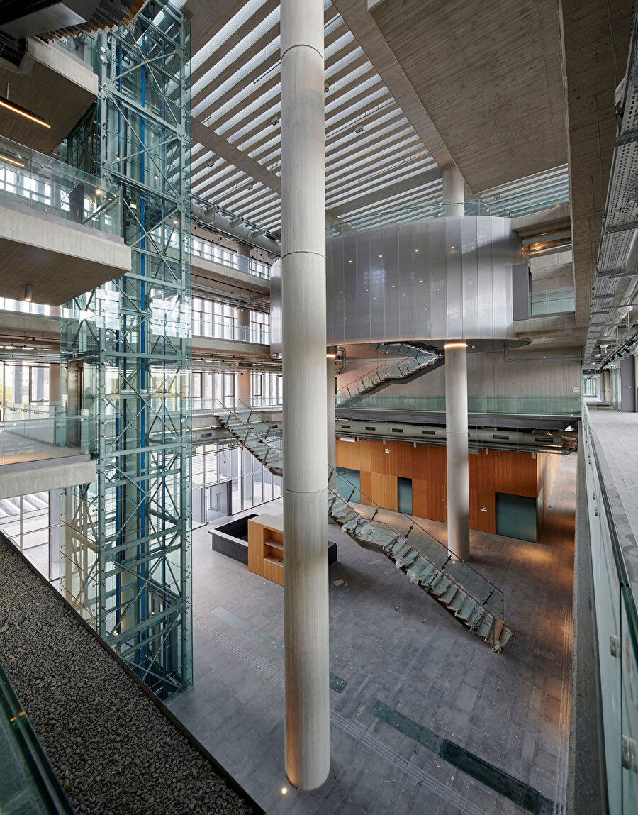 Merkezdeki kapalı avlu, daire kesitli kolonlar, ahşap ve brüt beton.