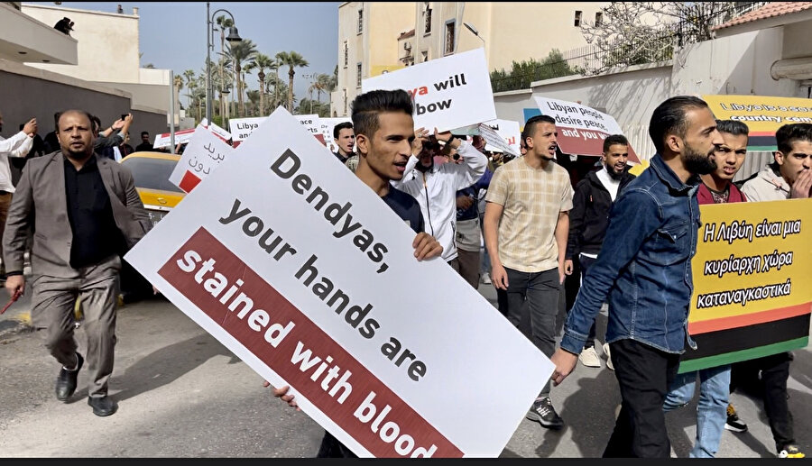 Libyalı bir protestocu elinde 'Dendias senin elinde kan lekesi var' yazılı bir pankart taşıyor.