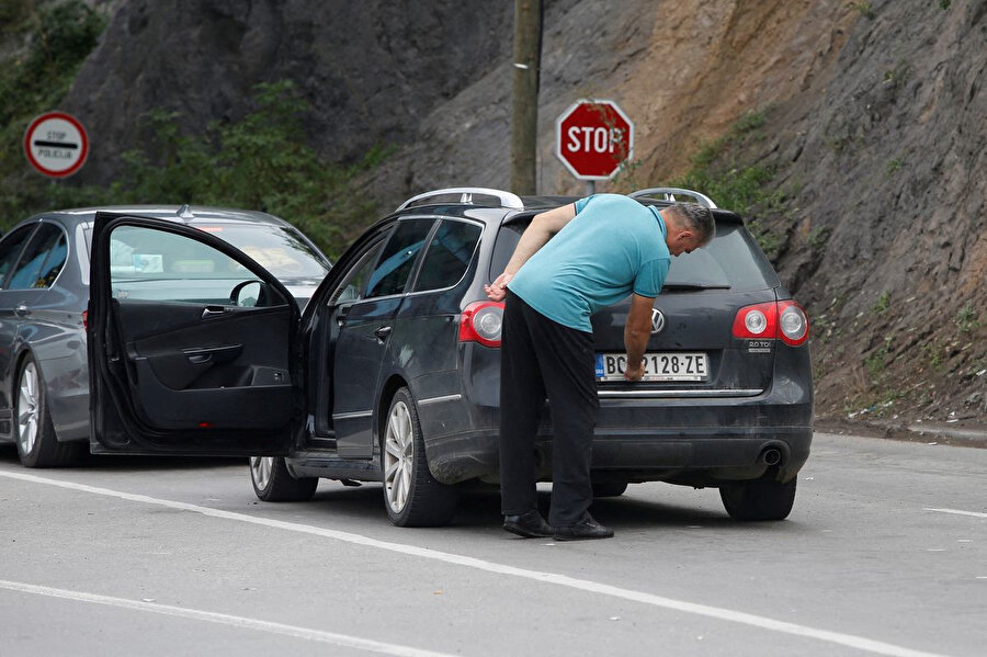 Kosova'daki Jarinje sınır kapısından geçen bir sürücü, plakasındaki ulusal işaretleri kapsayan bir çıkartmayı çıkarıyor.