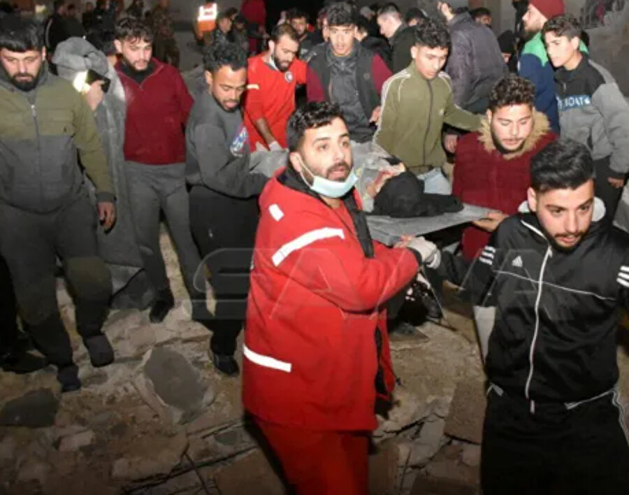 6 Şubat 2023'te kurtarma ekipleri Suriye'nin Hama kentinde meydana gelen depremin ardından çöken bir binanın bulunduğu yerde sedyeyle bir kişiyi taşıyor.