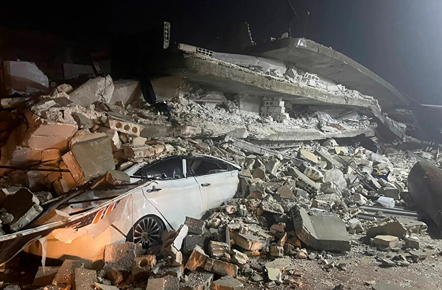 Suriye'nin kuzeyindeki İdlib eyaletine bağlı Azmarin kasabasında çöken bir binanın enkazı altında bir otomobil görülüyor.