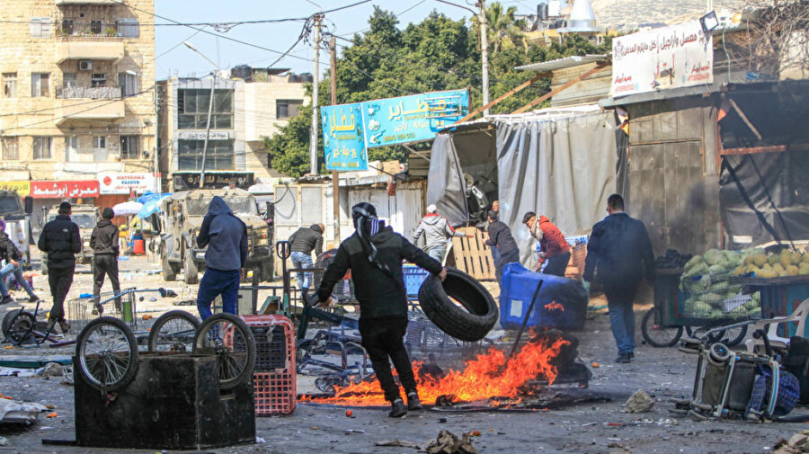 Filistinli gençler, işgal altındaki Batı Şeria'nın eski Nablus kentindeki sebze pazarındaki çatışmalar sırasında İsrail ordusuna ait aracın önünde lastik yakarken, 23 Şubat 2023.