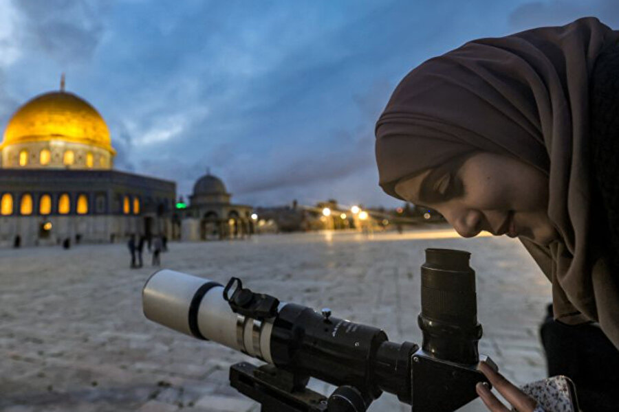 El-Aksâ yerleşkesindeki Kubbetu's-Sahra türbesinin yakınında İslam'ın kutsal ayı Ramazan'ın başlangıcını kutlamak için teleskopla gökyüzündeki ayı kontrol eden bir kadın.