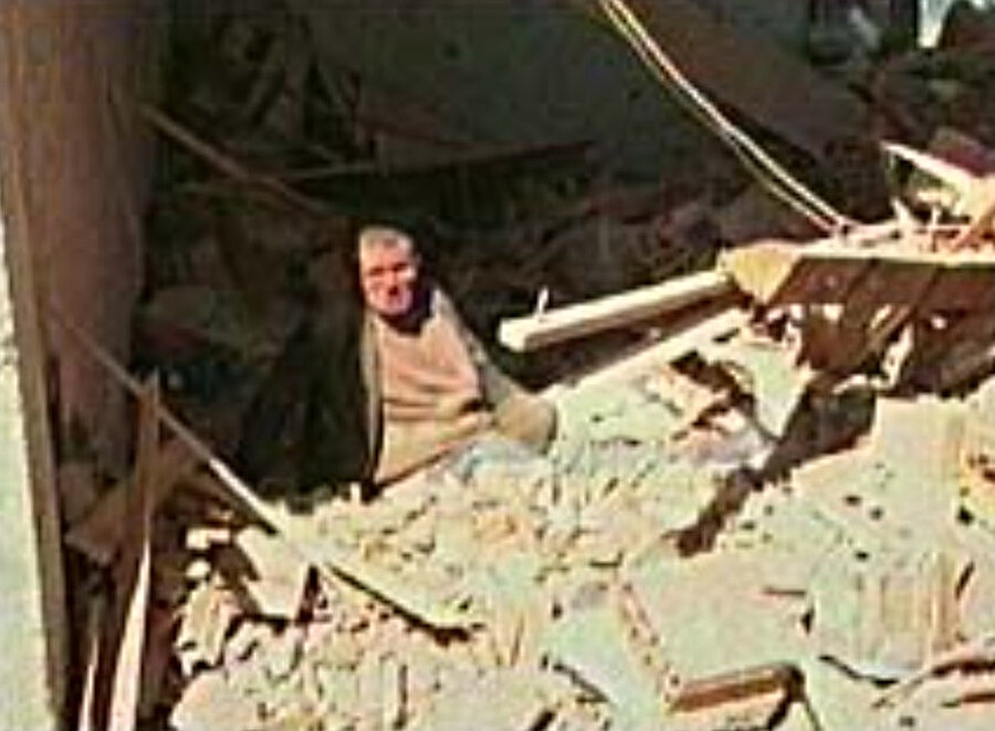 Bir adam, konvoyların vurulduğu yerin yakınındaki evinin enkazında oturuyor.
