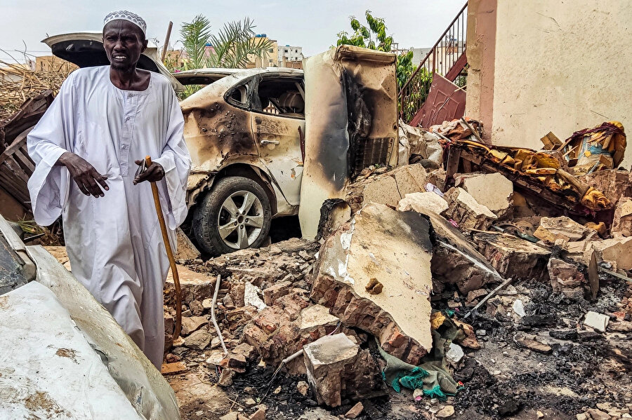 Top mermisi isabet eden bir evin dışındaki molozların arasında yürüyen Sudanlı adam, hasarı inceliyor.