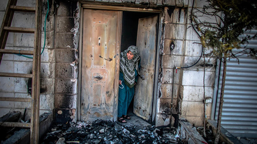 İsrailli yerleşimcilerin gerçekleştirdiği saldırı sonrasında dış cephesi yanmış evinden çıkan Filistinli bir kadın.