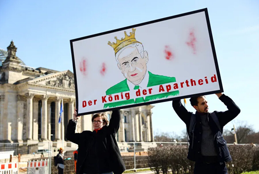 Protestocular, Almanya ziyareti sırasında İsrail Başbakanı Benjamin Netanyahu'yu protesto ederken 'Apartheid Kralı' yazan bir poster taşıyor.