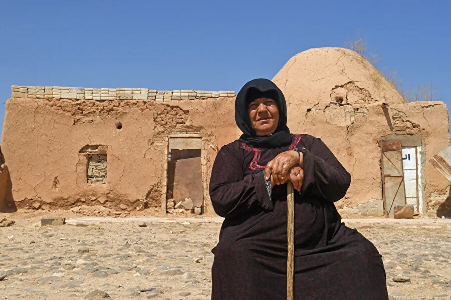 Akla köyündeki geleneksel kerpiç evinin önünde oturan bir kadın.