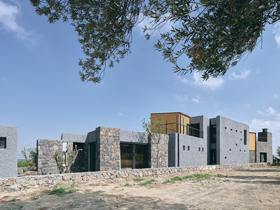 Taş ve beton kullanılarak yapılan zemin kat ile hafif ahşap karkastan yapılan üst kat arasında belirgin bir kontrast oluşturuluyor.