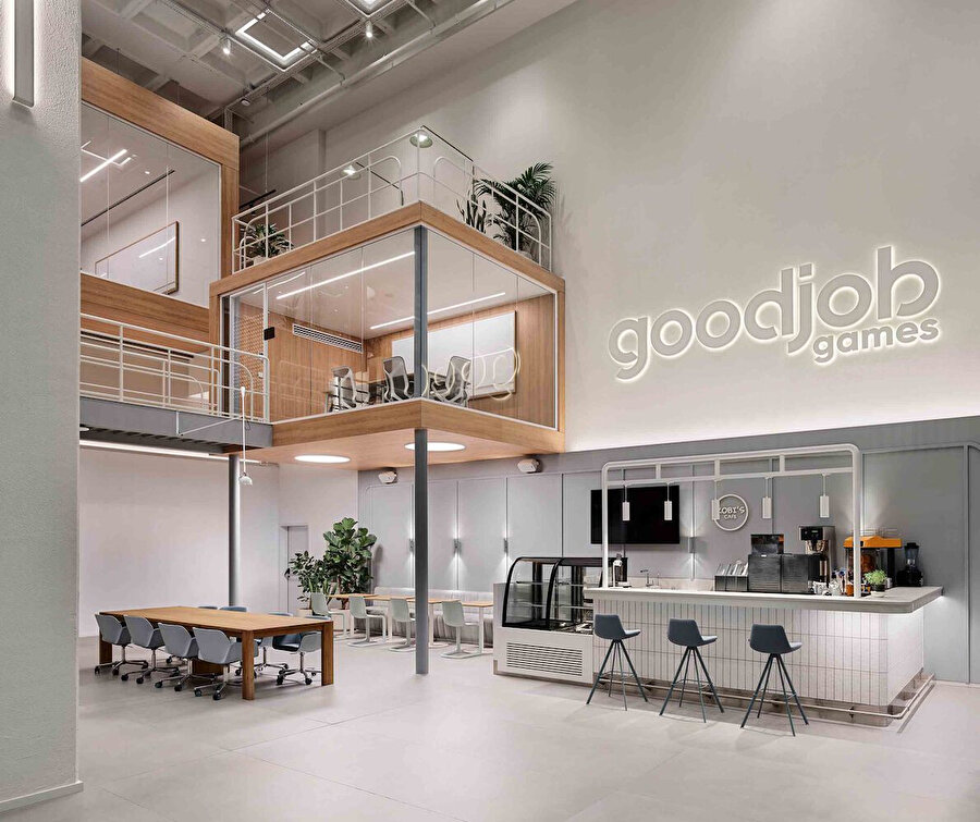 Kafe bölümü, asma kattaki toplantı alanları ve beyaz duvarlarında aydınlatmalı logo tasarımıyla marka kimliğini yansıtıyor. 