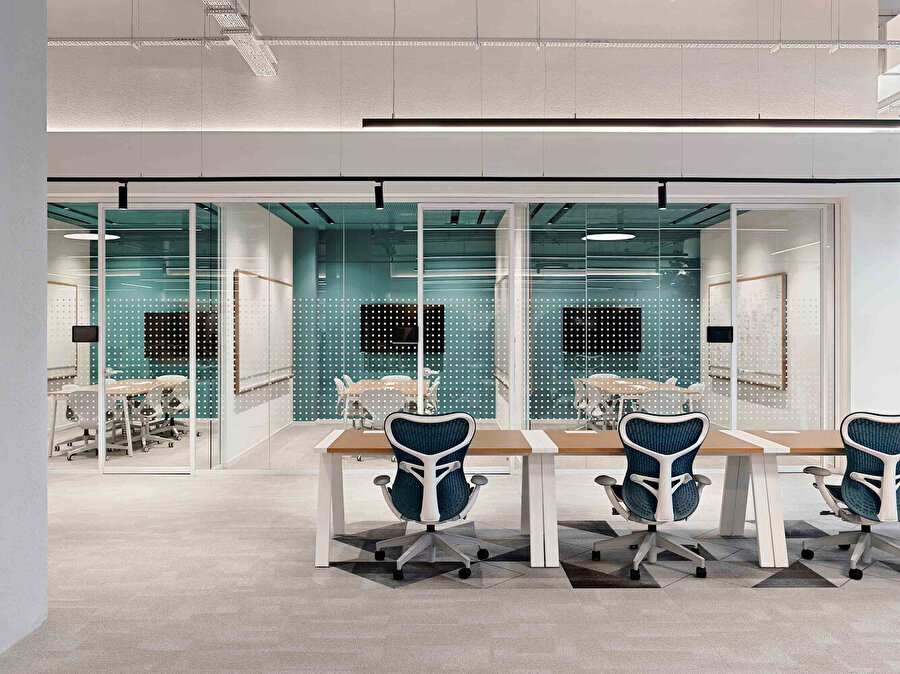 Çalışma alanları, noktalı cam bölücüler ve ergonomik mobilyalarla modern bir ofis ortamı sunuyor.