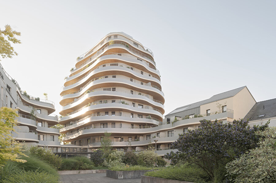 Binanın dalgalı formları kentsel dokuya dinamik bir karakter katarken zemin kattaki ahşap detaylar ve beyaz yüzeyler yapının sokakla kurduğu ilişkiyi güçlendiriyor.