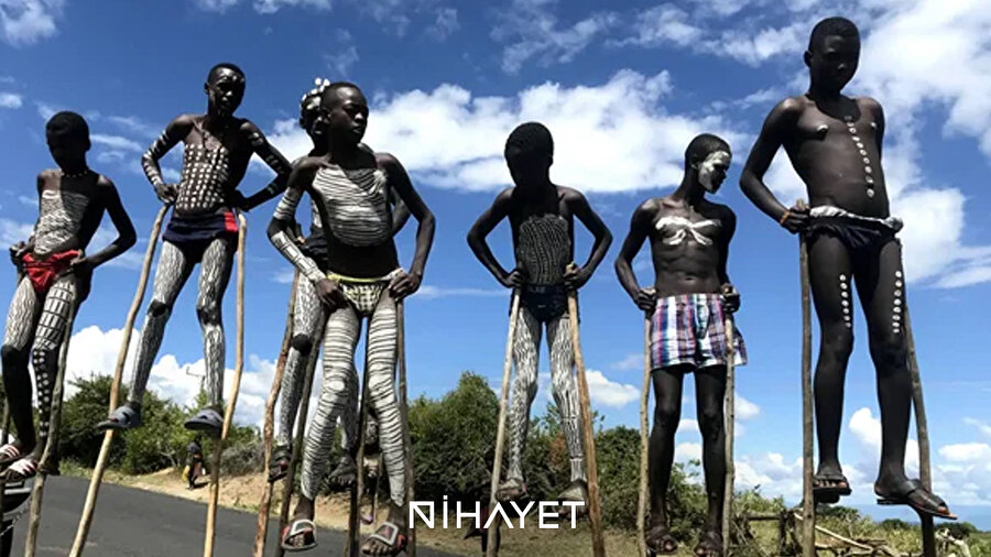 👀 Etiyopya’nın Omo Vadisi’nde yaşayan Banna Kabilesi çocuklarının, uzun sırıklar üzerinde metrelerce yüksekte yürümesi sadece etkileyici bir akrobasi değil, hayati bir zorunluluktur.