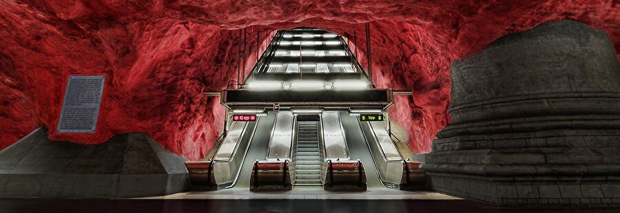 Radhuset İstasyonu-İsveç
İsveç'in başkenti Stockholm'de bulunan metro hattındaki Radhuset İstasyonu, tasarımıyla birçok duraktan oldukça farklı. Doğal mağara yapısı bozulmadan inşa edilen istasyon 1950'lerden bu yana hizmet veriyor. Kayaların görüntüsünü daha dikkat çekici göstermek için istasyon içinde özel ışıklandırmalar kullanılıyor. Ayrıca istasyon, dünyanın en uzun sanat merkezi olma özelliğini taşıyor. Yolcular 110 kilometrelik yolculuk boyunca 150'den fazla sanatçının heykel, resim ve kabartmalarının yer aldığı sergiye görebiliyor.