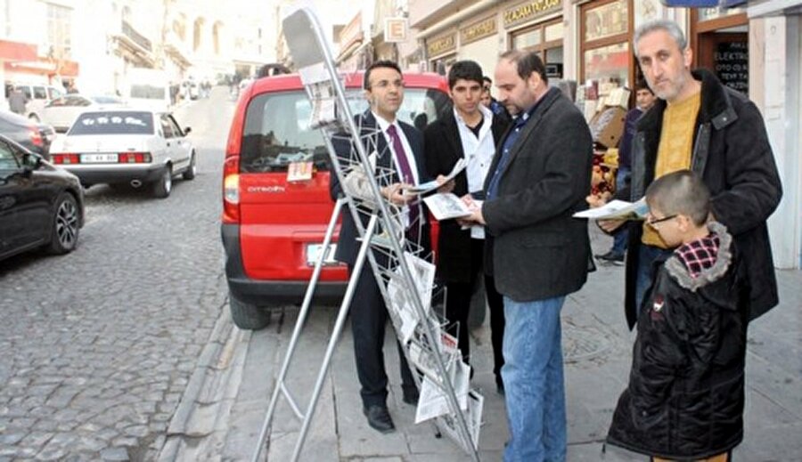 Gazete bayiinin önünde durup tezgâhtaki gazeteleri ayaküstü okurlar.
