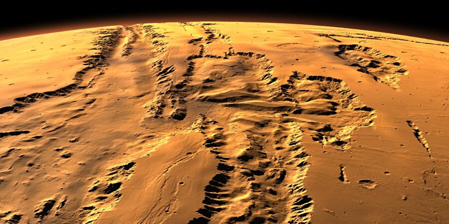 İlerleyin, Valles’e varacaksınız
Güney batı istikametine doğru ilerlediğinizde Valles Marineris'e varırsınız; bu büyüleyici vadi Mars'ın ekvator çizgisinde 4000 km uzunlukta derin bir yara gibidir. Bazı yerlerde 7 km'ye varan derinliğiyle Grand Canyon'dan dört kat daha derindir. Bunun nasıl oluştuğu ise bilinmiyor. Rengarenk tabakalar şeklindeki yapısı eski bir göl tabanındaki birikinti ya da yanardağ küllerinin birikmesi sonucu oluştuğuna işaret ediyor. Amerika'da erozyon sonucu oluşmuş kanyonun tersine, bu vadinin iki tarafının yapboz parçaları gibi birbirini tamamlaması tektonik plakaların birbirinden ayrılmasıyla bu yarığın oluştuğunu gösteriyor.