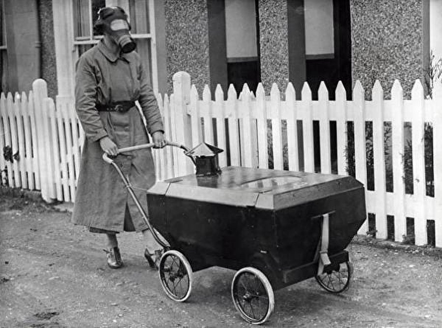 
                                    1938 yılında İngiltere'de bir kadın gaz maskesi takıyor. Ayrıca kadının ittiği kutu ise bebeklerin gazdan etkilenmemesi için üretilen özel bir bebek arabası.
                                