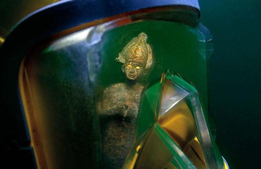 Bu dalıcı maskesinin yansımasında, Tanrı Osiris'in bronz bir heykelini görüyoruz. Taç iktidarın tipik işaretidir ve bu heykelin gözleri altın tabakalarla süslenmiştir.